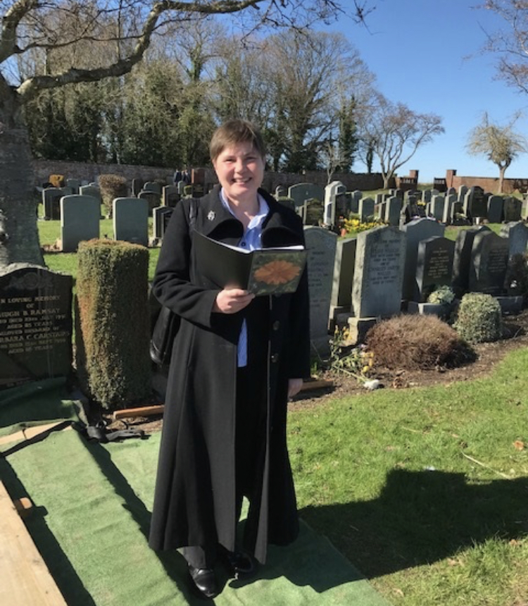 A woman standing in a graveyard holding a booklet of notes